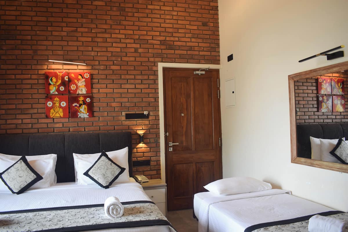 A hotel room with a brick wall, a wooden door, and a bed with white bedding and decorative pillows.