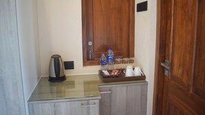 Een kleine kitchenette met een waterkoker, waterflesjes, glazen en een schaal met snacks.