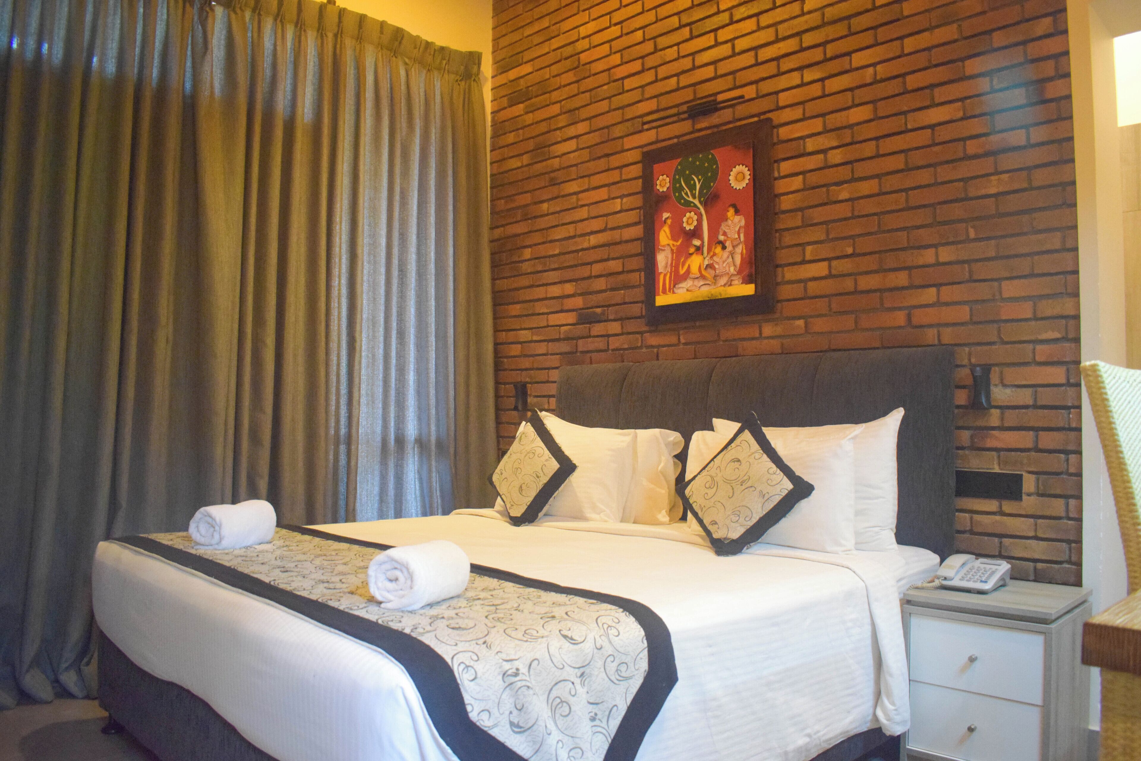 Een hotelkamer met een opgemaakt bed, een nachtkastje met telefoon en een bakstenen muur met een lijst erin.