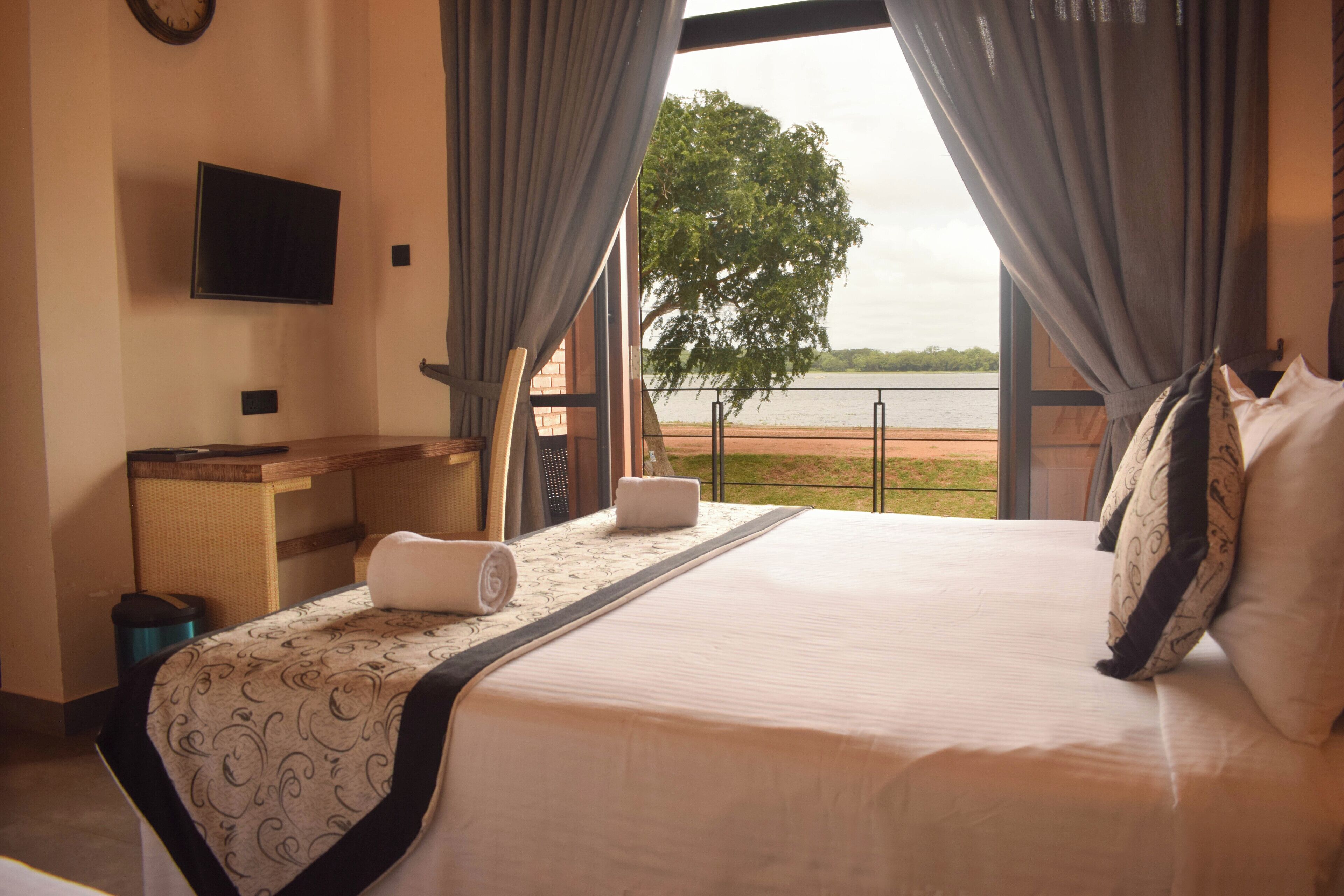 A hotel room with a bed, a desk, a television, and a view of a lake.