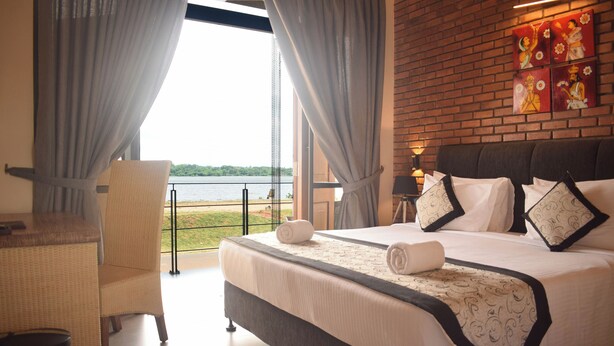 Een slaapkamer met een groot bed, een stoel, een klein tafeltje en uitzicht op het meer.