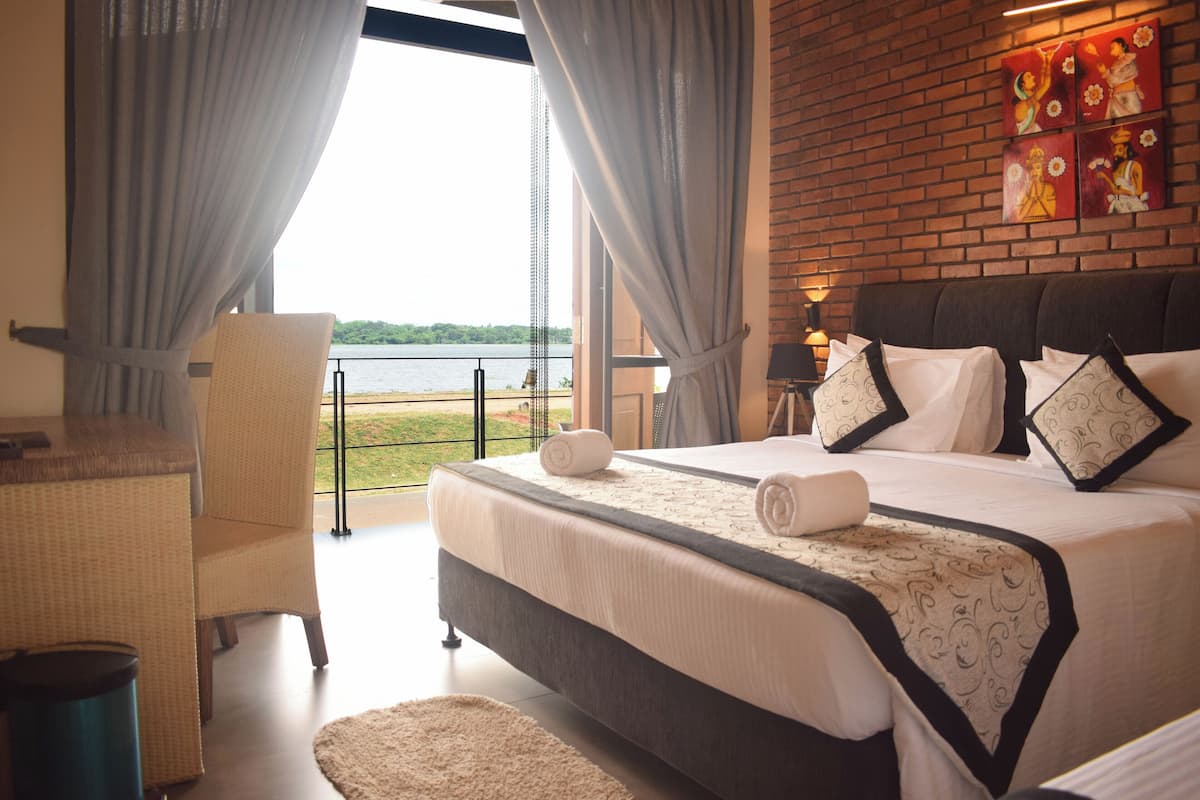 A bedroom with a large bed, a chair, a small table, and a view of the lake.