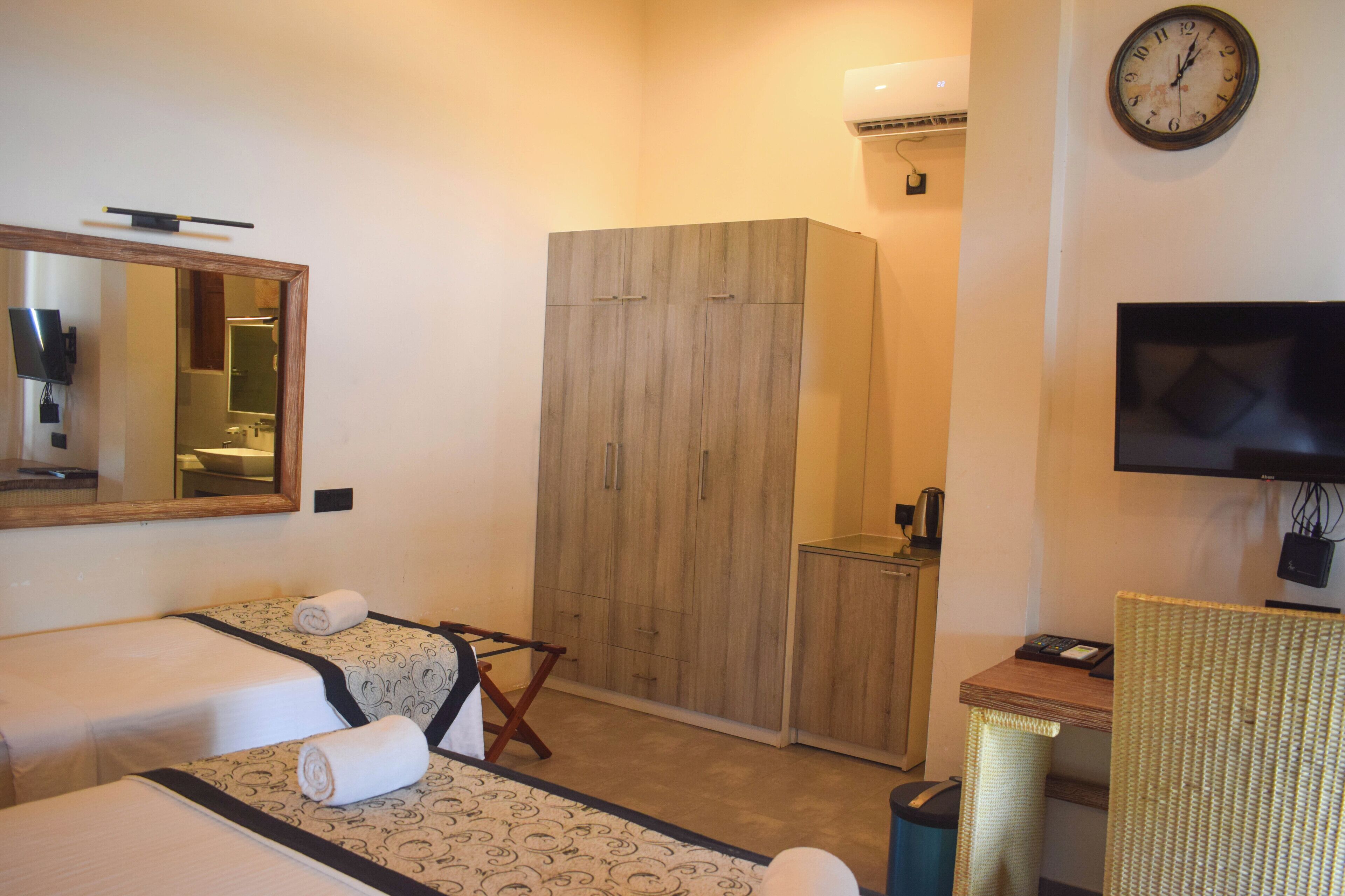 A hotel room with two beds, a wardrobe, a television, and a desk.