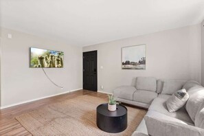 A living room with a grey sofa, a round black coffee table with a plant, and two framed pictures on the walls.