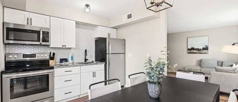 A modern kitchen with white cabinets, stainless steel appliances, and a black dining table.