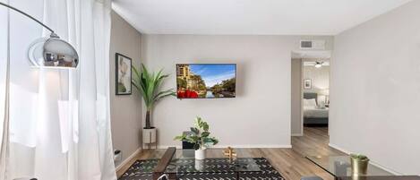 A modern living room with a sofa, a coffee table, a TV mounted on the wall, and a potted plant.
