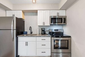 Una cocina moderna con electrodomésticos de acero inoxidable, armarios blancos y salpicadero de azulejos.