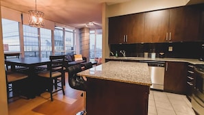 A modern kitchen with dark wood cabinets, a granite countertop, and a dining area with a black leather sofa and wooden chairs.