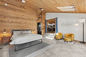 A modern bedroom with a wooden ceiling, a bed, a nightstand, a lamp, and a chair. - Luxe Lake Home | Hot Tub + Private Dock & Beach (Nine Mile Falls)