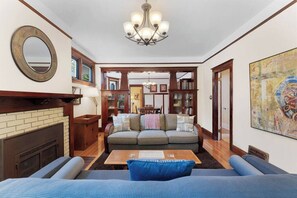 A living room with a fireplace, a sofa, a coffee table, and a chandelier. - Charming South Hill Craftsman—Porch, Chef’s Kitchen, Yard & BBQ (Spokane)