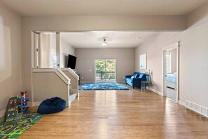 A spacious hallway with a blue rug, a blue sofa, and a staircase with a TV mounted on the wall.