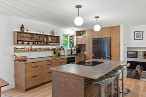 A modern kitchen with a central island, wooden cabinetry, and a built-in refrigerator. - Game On | 2 Lounges, Ping Pong, Firepit + Hot Tub (Spokane)