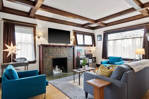 Ein Wohnzimmer mit Kamin, blauen Sofas, einem Fernseher und Holzbalken an der Decke.