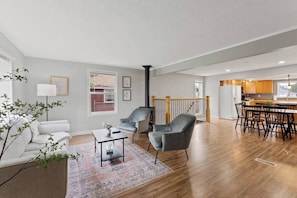 En rummelig opholdsstue med sofa, stole, spisebord og et køkken i baggrunden.