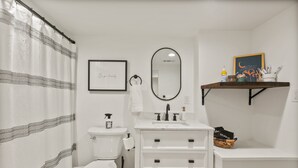 Un baño con inodoro, lavabo, espejo y estante con artículos de aseo.