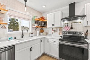 A modern kitchen with white cabinets, a stainless steel oven, and a microwave on a wooden shelf. - Family- & pet-friendly Spokane home: 3BR/2BA, fenced yard, near downtown. (Spokane)