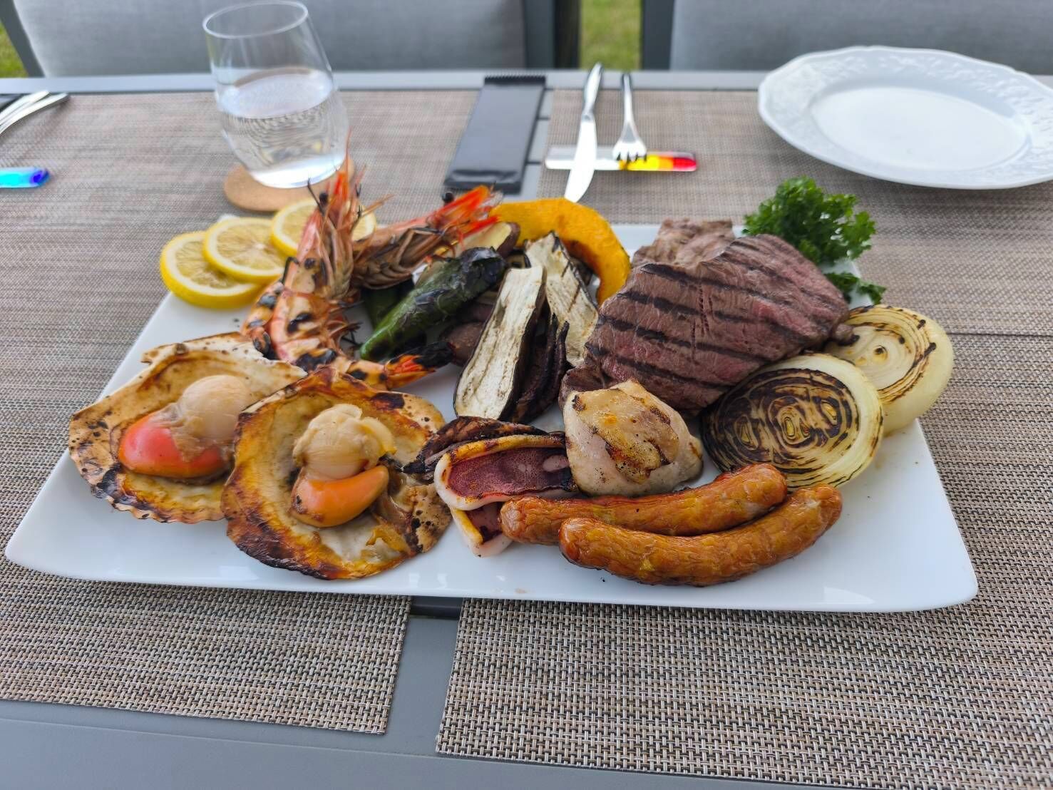 A plate of grilled food including steak, sausages, grilled vegetables, and seafood.