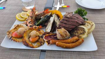 A plate of grilled food including steak, sausages, grilled vegetables, and seafood.