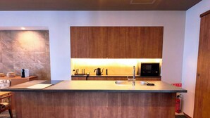 Une cuisine moderne avec des meubles en bois, un îlot central doté d’un évier, d’un four à micro-ondes et d’une bouilloire.