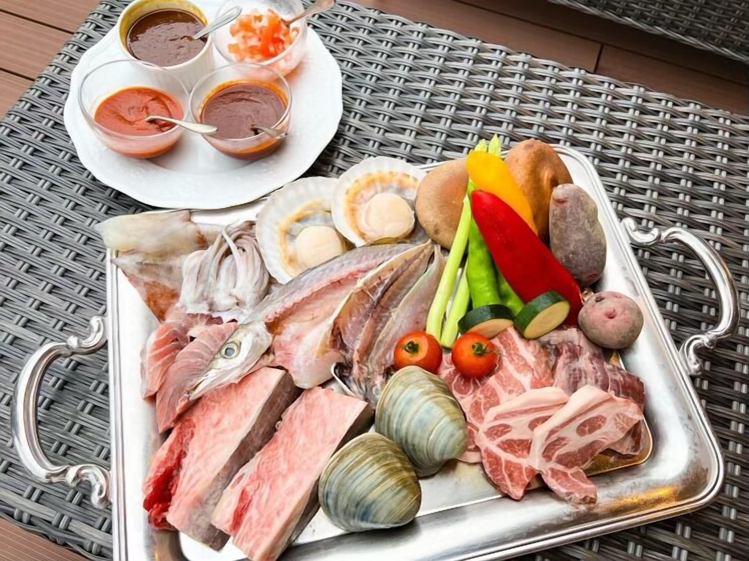 A tray of raw meats, vegetables, and seafood on a metal plate.