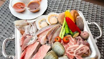 A tray of raw meats, vegetables, and seafood on a metal plate.