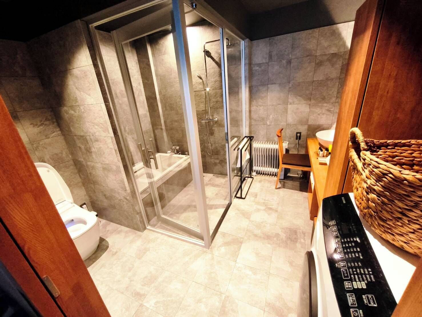 A bathroom with a glass-enclosed shower, a toilet, a radiator, and a wooden chair.