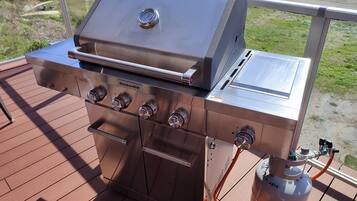 Een roestvrijstalen buitenbarbecue met vier branders en een ingebouwde thermometer, aangesloten op een propaantank.