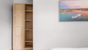 Une chambre avec une armoire en bois, un lit et un tableau représentant un paysage côtier, encadré et accroché au mur.