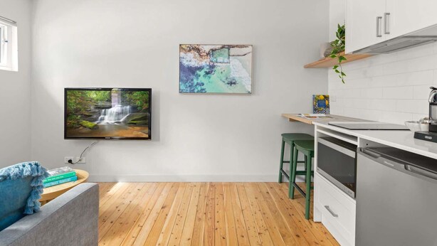 Une cuisine moderne équipée d’un téléviseur à écran plat, d’un plancher en bois et d’un tabouret vert.