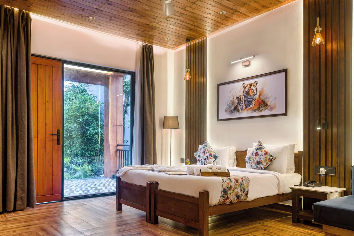 A spacious bedroom with a large bed, a wooden headboard, a framed tiger artwork, and a view of greenery through a sliding door.