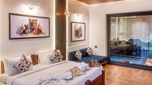 A hotel room with a large bed, a seating area with a view, and artwork on the walls. - Corbett Machaan Resort (Ramnagar)