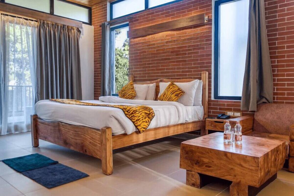 A wooden bed with white bedding and tiger-patterned pillows, a wooden nightstand, a wooden coffee table, and a view of a brick wall and windows.