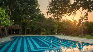 A swimming pool with a tiled deck, surrounded by trees and a sunset in the background. - Corbett Machaan Resort (Ramnagar)