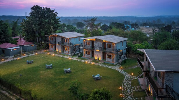 A two-story building with a stone facade, multiple balconies, and a well-maintained lawn with outdoor seating. - Corbett Machaan Resort (Ramnagar)