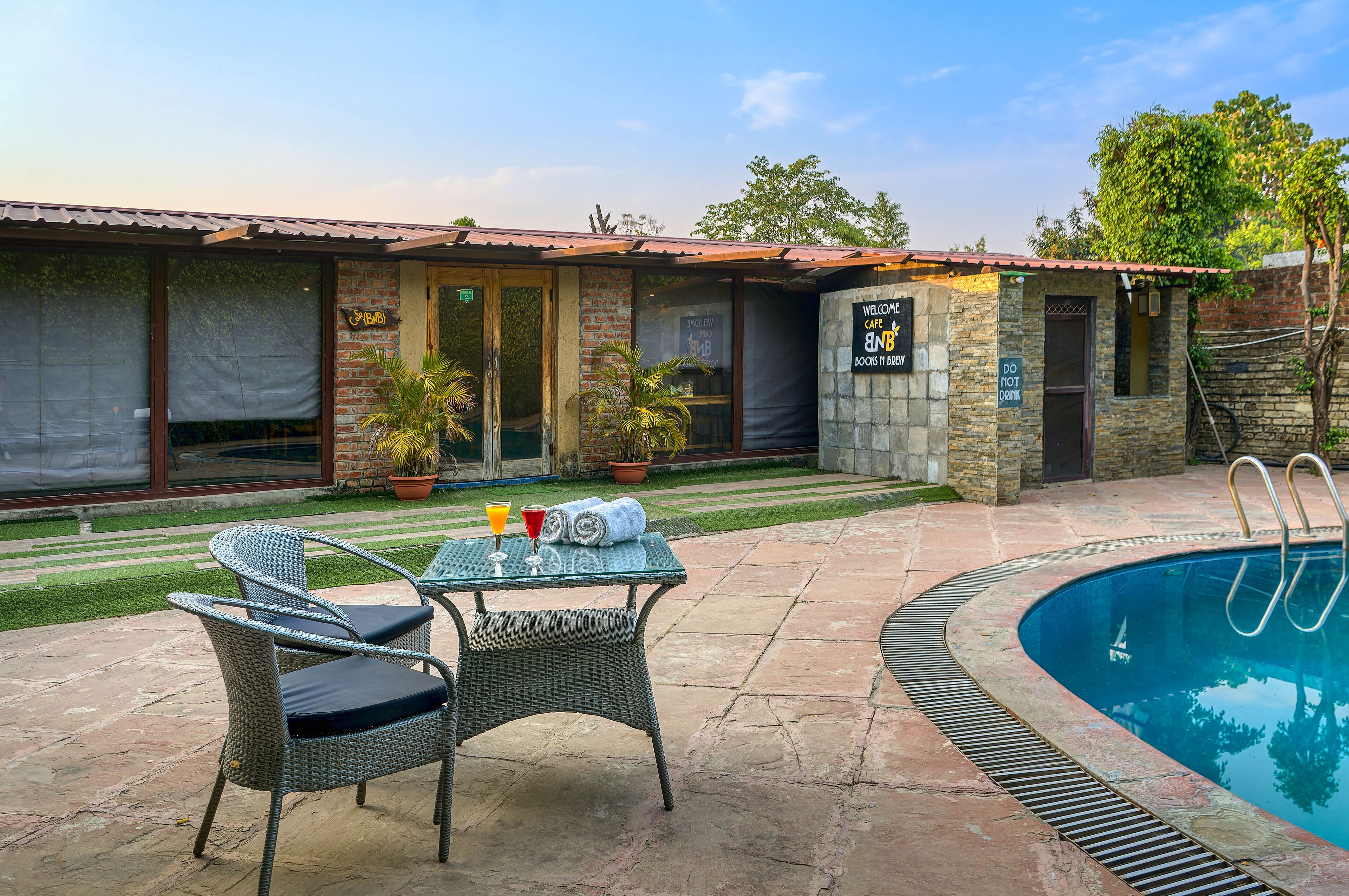 A pool area with wicker chairs and a table, a brick building with a sign, and a clear sky.