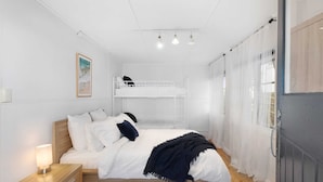 Ein Schlafzimmer mit einem hölzernen Bett, einem Nachttisch, einem weißen Kleiderschrank und einem Hochbett darüber.