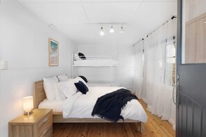 Ein Schlafzimmer mit einem hölzernen Bett, einem Nachttisch, einem weißen Kleiderschrank und einem Hochbett darüber.