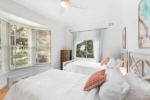 Ein Schlafzimmer mit zwei Betten, einem Deckenventilator und großen Fenstern mit Jalousien.