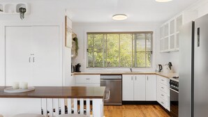 Eine moderne Küche mit weißen Schränken, einem Holztisch und einem Fenster mit Jalousien.
