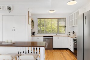 Eine moderne Küche mit weißen Schränken, einem Holztisch und einem Fenster mit Jalousien.