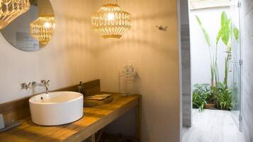 A bathroom with a round sink, wooden vanity, and two hanging light fixtures.