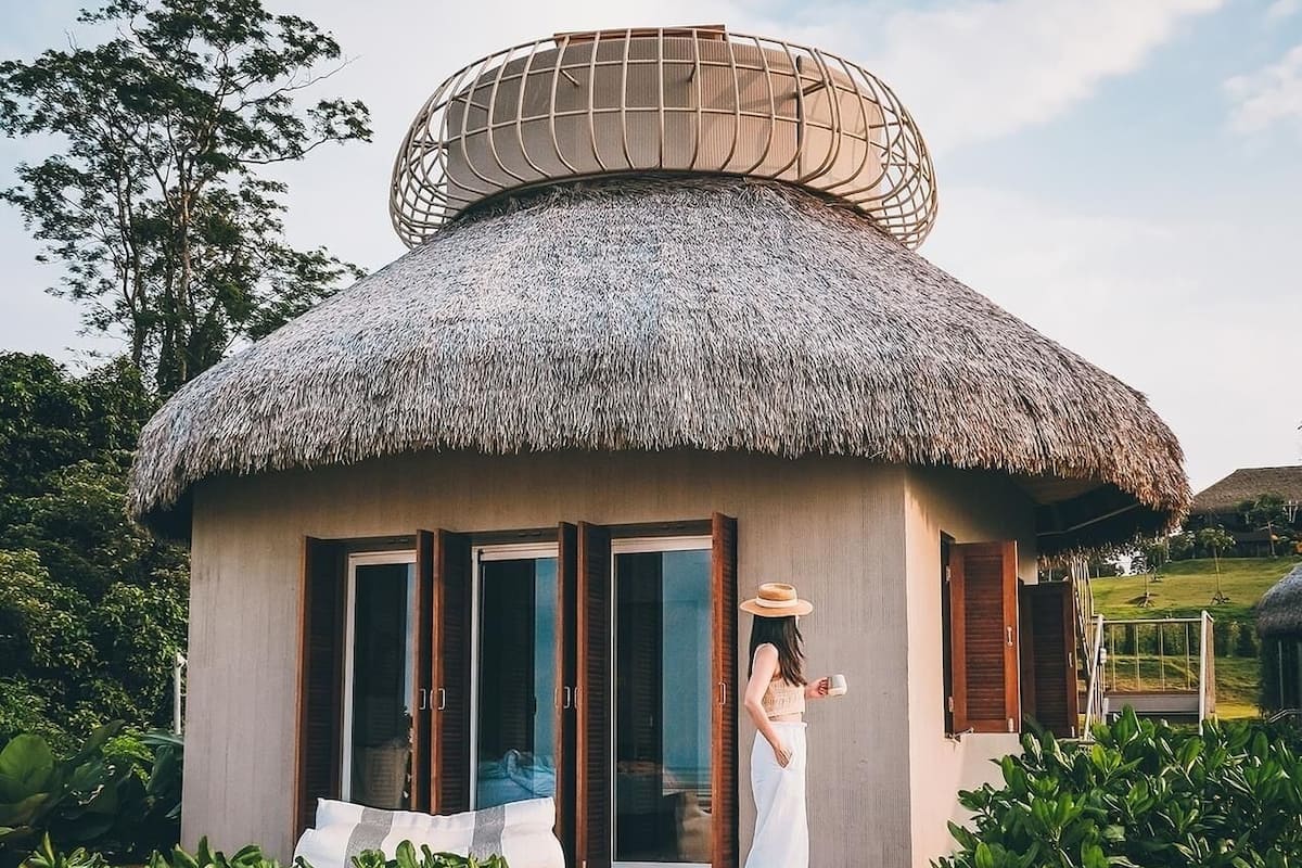 A thatched-roof structure with a large circular opening at the top, a wooden door, and a glass window.