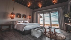 Ein Schlafzimmer mit einem großen Bett, einem kleinen Tisch und Blick auf den Strand.