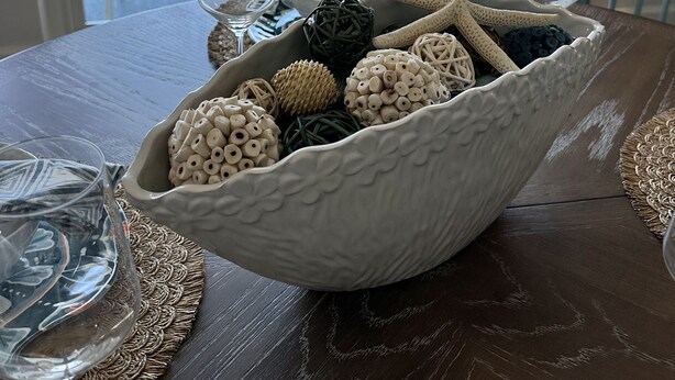 A dining table with a white bowl filled with decorative items, a view of the ocean and palm trees through a window, and a chair. - 10 Steps to the Sand…Capitola Beach Front at the mouth of the Wharf-Pet Friendly (Capitola)