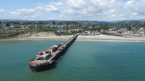 A pier extending into a calm sea with a beach and residential area in the background. - 10 Steps to the Sand…Capitola Beach Front at the mouth of the Wharf-Pet Friendly (Capitola)