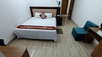 A hotel room with a bed, a blue armchair, a wooden desk, and a door.