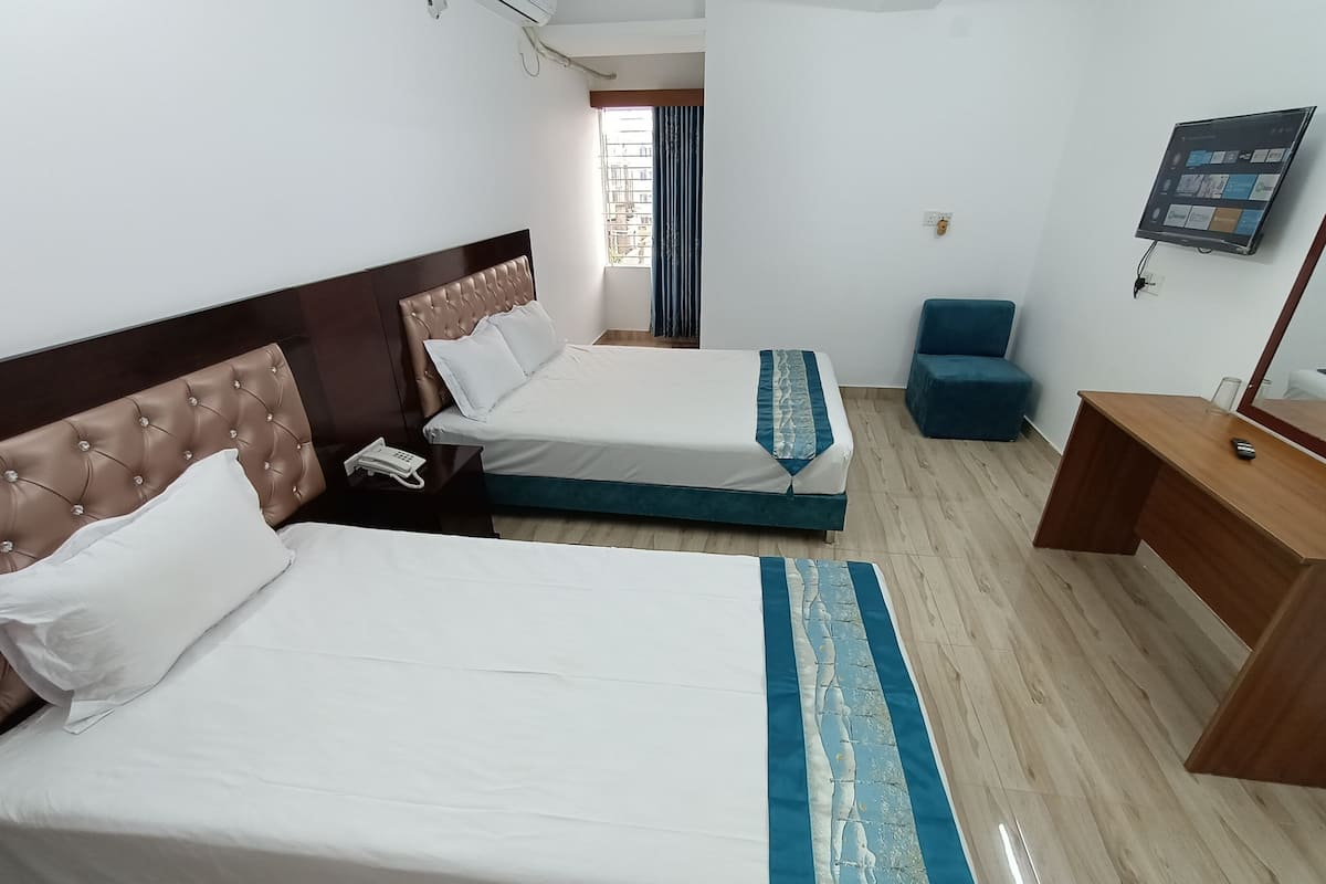 A hotel room with two beds, a desk, a chair, and a TV.