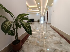 A long, well-lit hallway with a marble floor, potted plants, and a television on the wall. - Hotel D-Palace (Dhaka)