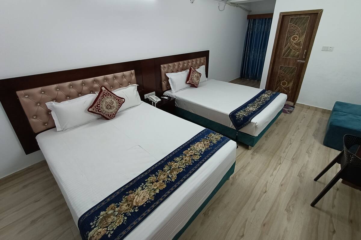 A hotel room with two beds, a desk, a chair, and an air conditioning unit.