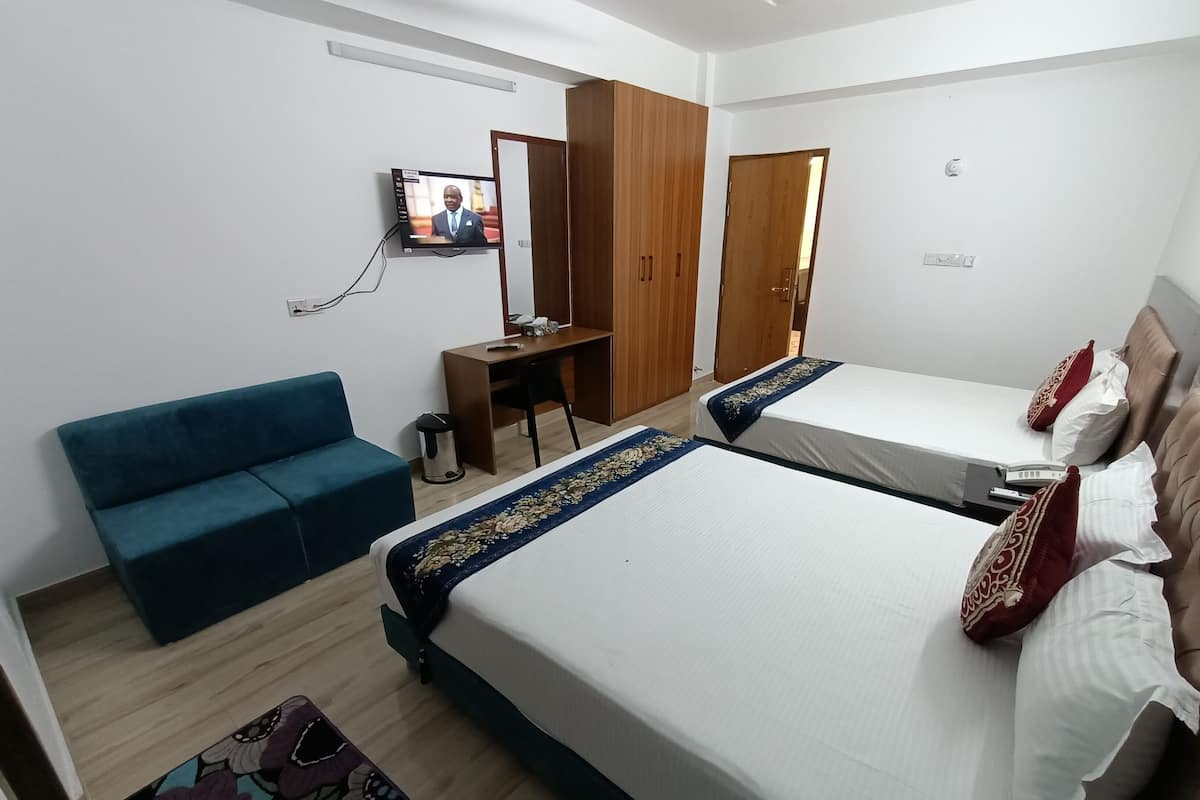 A hotel room with two beds, a desk, a blue sofa, and a television on the wall.